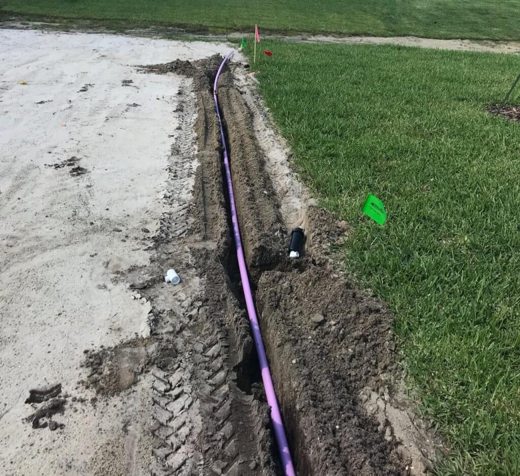 Purple reclaimed water irrigation line installed in a freshly dug trench along a lawn and sand area, part of a Pro Lawn Turf & Landscape irrigation project.