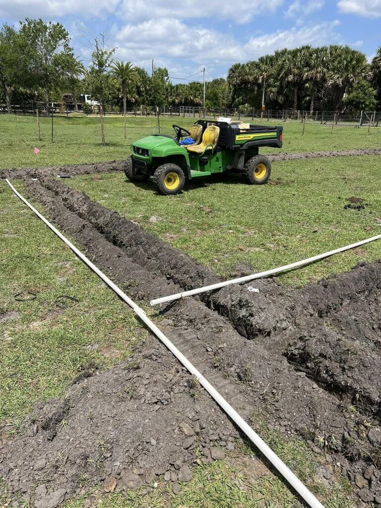 Trenches being dug and irrigation pipes laid out on a grassy field, with a green utility vehicle on site, part of a landscaping project by Pro Lawn Turf & Landscape.